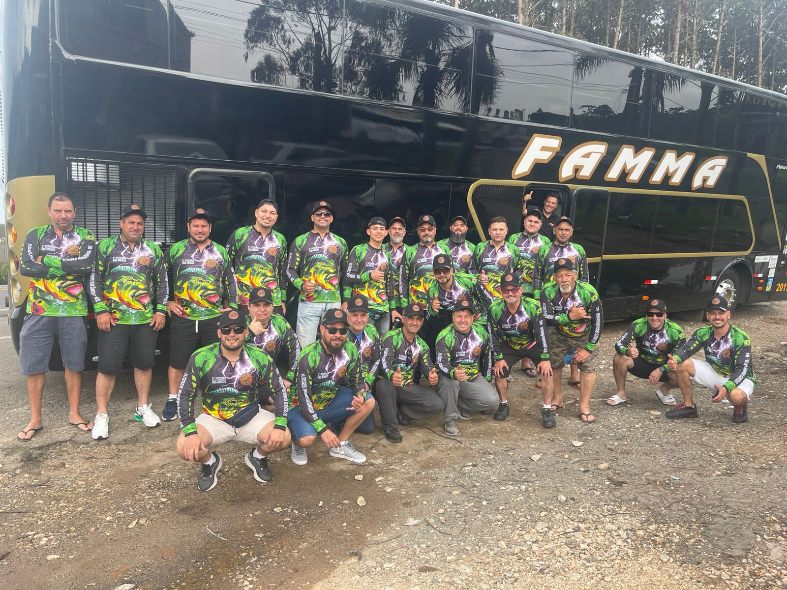 Grupo de homens uniformizados para pescaria posando em frente ao ônibus da Famma Turismo antes de iniciar uma viagem de pesca.